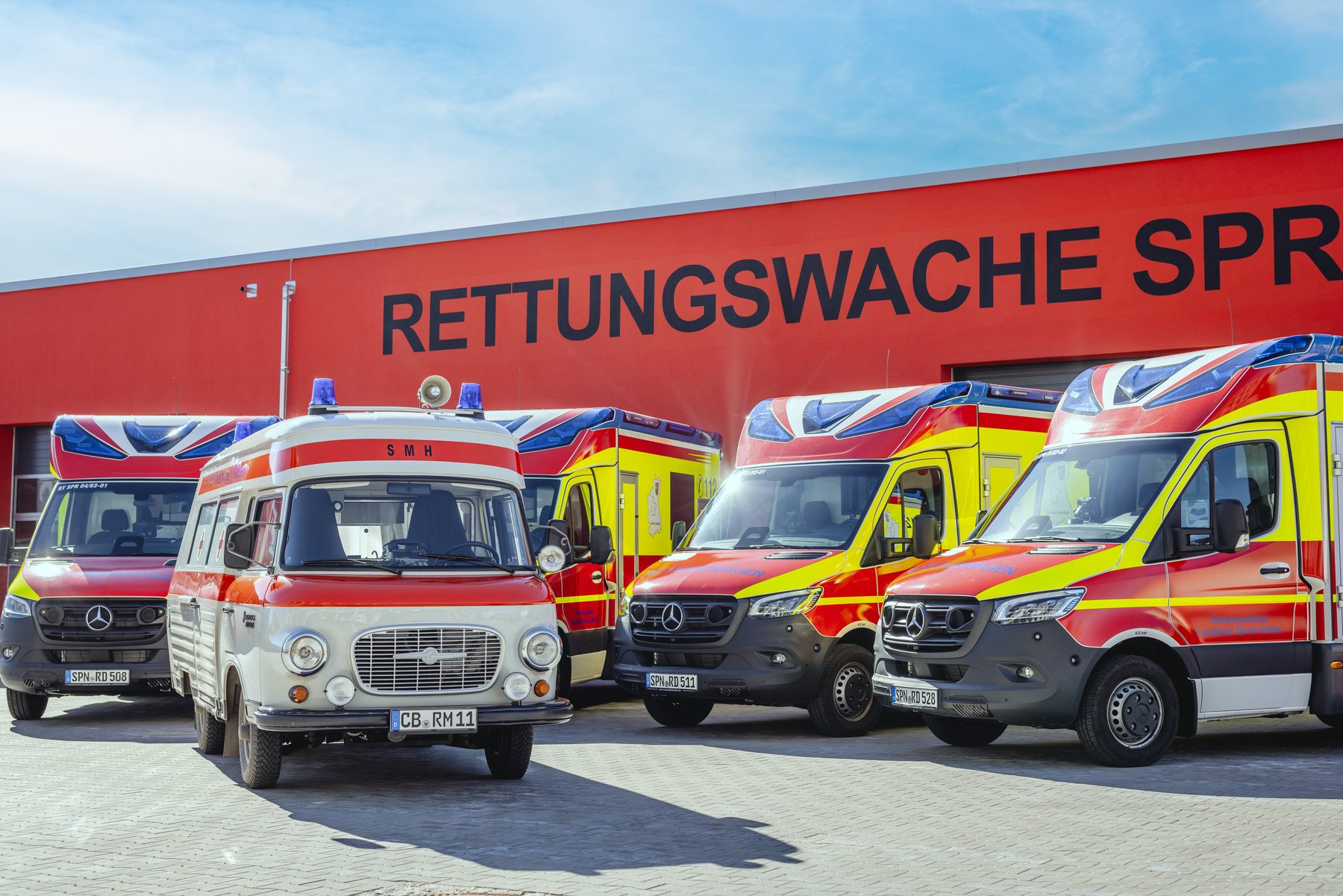 Historischer Krankenwagen und moderne Rettungswagen in Reihe vor der Rettungswache